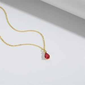 Detailed close-up of a red pear-cut glass droplet pendant on a delicate gold chain