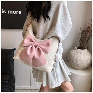 Close-up of cream shoulder bag featuring a large pink bow and hybrid chain strap