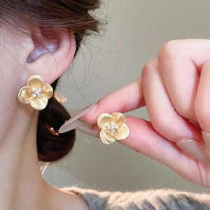 Close-up of matte gold flower earrings with sparkling zircon centers on a model