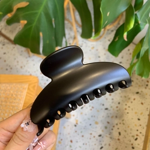 Close-up of matte black hair claw clip with rounded crescent design in hand