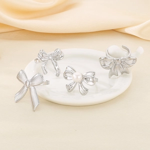 Close-up of assorted stainless steel bow rings with pearls on elegant white silk fabric