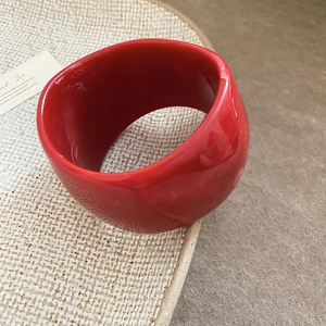 Macro detail of a wide red resin bangle with a polished finish on a minimalist tray