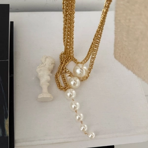 Detail of multi-layer gold chain necklace with white pearls on a white statue background