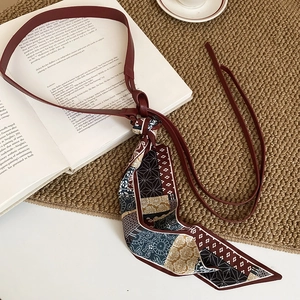 Macro shot of vintage burgundy leather belt with a patterned silk scarf and floral tassels