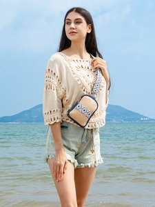 Bohemian straw crossbody phone bag with blue contrast trim and tribal wide strap on a beach