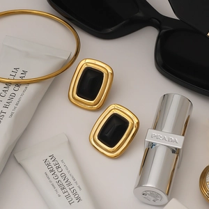 Flat lay of vintage gold-plated rectangular earrings with black stones and fashion props