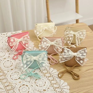 Kids straw crossbody bags with lace bows in pink cream and blue colors on wooden desk