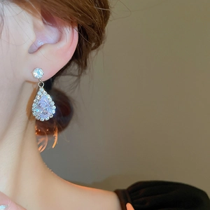 Close-up of elegant silver zircon teardrop earrings worn by a model in soft lighting