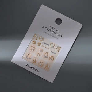 Golden geometric nail art charms with pearls on white backing card, 45-degree angle view