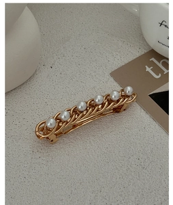 Close-up of golden metal chain hairpin with seven white pearls on beige background