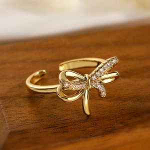 Elegant gold bow open ring with cubic zirconia stones on dark wood background