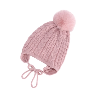 Detail view of pink cable knit baby hat with soft faux fur pompom and earflap straps