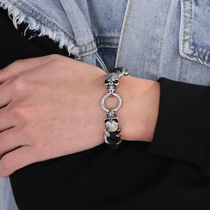 Detailed view of men's skull bracelet with woven leather and stainless steel on denim