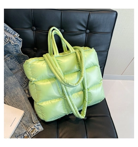 Dettaglio della borsa tote trapuntata verde erba lucida su un divano in pelle nera