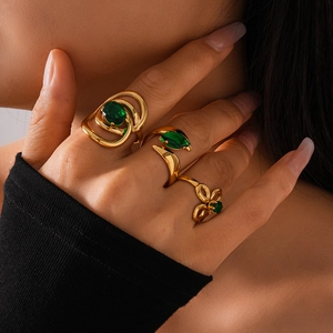 Detailed close-up of gold spiral rings with emerald green zircon gemstones worn by a model