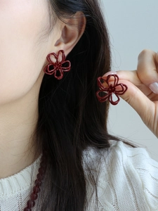 Nahaufnahme eleganter hohler dunkelroter Blumenohrringe an einem Model im minimalistischen Stil