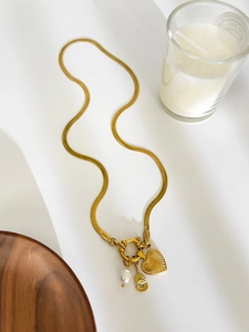Close-up of golden snake chain with heart, letter S and teardrop pearl charms