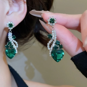 Close-up of tassel earrings featuring green heart stones and sparkling floral accents