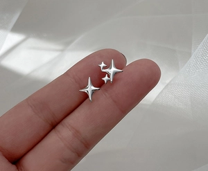 Close-up of silver four-pointed star earrings held to show scale and metallic texture