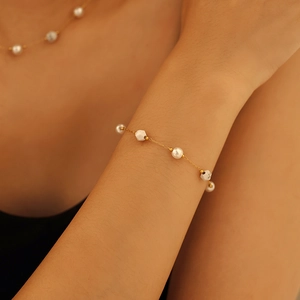 Bracelet doré élégant avec perles blanches et perles géométriques porté au poignet