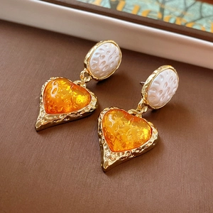 Detail of vintage gold earrings with textured white oval and amber heart pendant charms