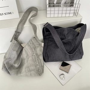 Close-up of oversized tie-dye denim tote bags in light grey and deep blue on a white stand