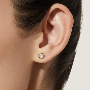 Close-up of minimalist gold-plated round mother of pearl stud earrings on a model's ear