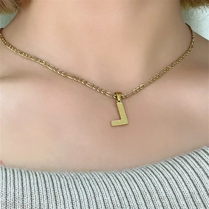 Primo piano di una collana a catena Figaro dorata con un ciondolo a lettera L su modella