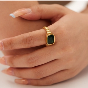 Detail of 18K gold-plated twisted ring featuring a large emerald-cut green gemstone