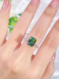 Macro shot of an emerald-cut green gemstone ring with pavé diamond band on a finger