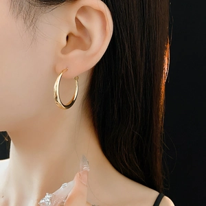 Close-up of elegant gold round hoop earrings worn by a model against a dark background