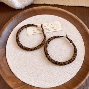 Close-up of leopard print velvet round hoop earrings on a warm wooden display tray