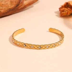 Détail rapproché d'un bracelet jonc en acier titane doré avec motif matelassé et strass