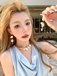 Close-up of shell and pearl necklace set worn by a model in a resort-style setting