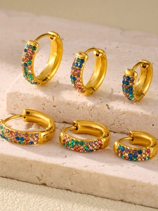 Macro shot of three pairs of gold turquoise and crystal inlaid hoop earrings on stone