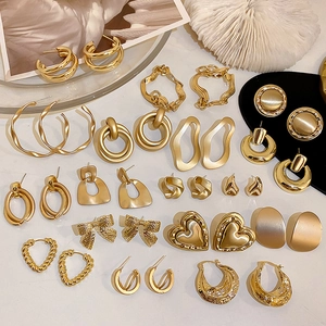 Flachbild von mehreren goldenen geometrischen Ohrringen und Herzformen auf Muschelhintergrund