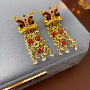 Dettaglio di orecchini a forma di leone dorato con smalto e nappe di perline rosse