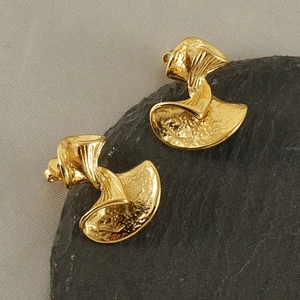Macro detail of golden bow earrings with hammer texture on black stone pedestal