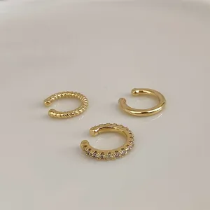 Détails de trois bagues d'oreille dorées aux styles lisse, torsadé et serti de zircons