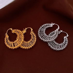 Detail view of large gold and silver woven hollow metal hoop earrings on textured fabric