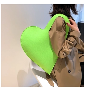Macro view of neon green oversized heart-shaped felt handbag worn by a model