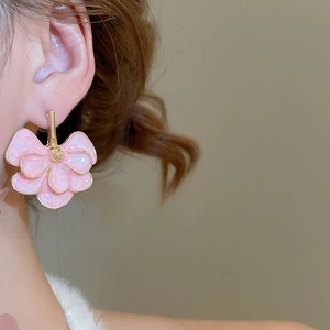 Close-up of pink flower petal earrings with gold trim worn on a model's ear lobe