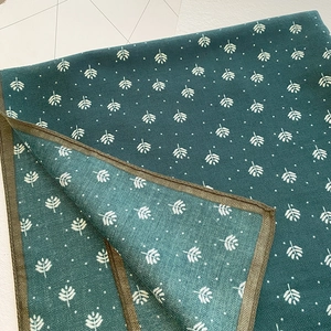 Detail of dark green printed scarf with leaf patterns and herringbone knit texture