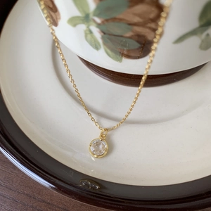 Detail of a minimalist gold necklace with a round crystal pendant on a ceramic plate