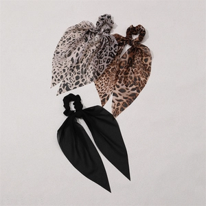 Fashionable leopard print and solid black bow scrunchies with long ribbons on beige surface