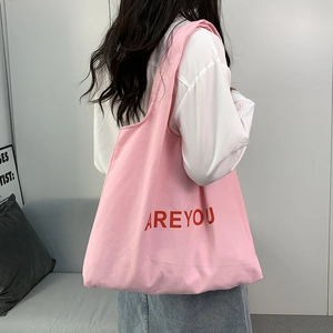 Detailed back view of pink canvas tote bag with red ARE YOU print on a model shoulder