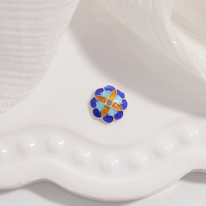 Vue macro d'une perle fleur en argent S925 émaillé bleu et orange sur porcelaine blanche