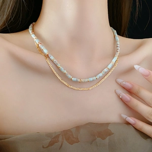 Close-up of a layered ethnic necklace with blue beaded stones and a gold chain on model