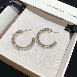 Detailed close-up of C-shaped silver earrings with hammered texture in a gift box