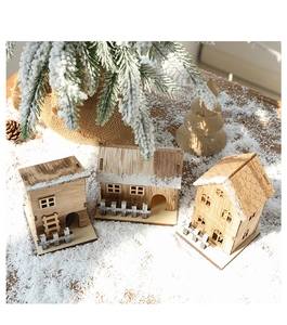 Miniature wooden Christmas house scene with LED lights and trees on artificial snow